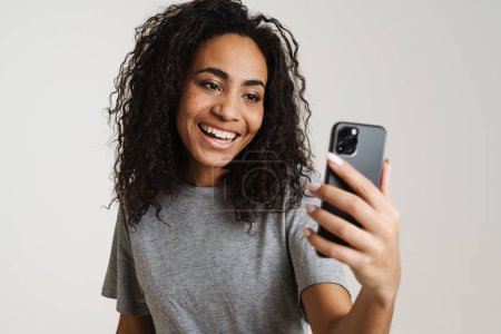 Foto de Joven mujer negra usando teléfono móvil y riendo aislado sobre fondo blanco - Imagen libre de derechos