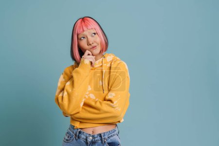 Photo for Asian girl with pink hair and piercing frowning while looking aside isolated over blue background - Royalty Free Image