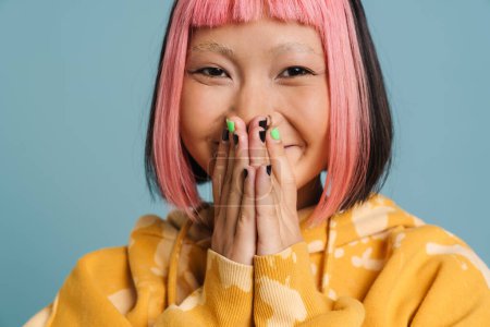 Téléchargez les photos : Asiatique fille avec rose cheveux rire et couvrant sa bouche isolé sur fond bleu - en image libre de droit