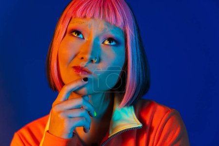 Photo for Asian puzzled girl with pink hair and piercing looking upward isolated over blue background - Royalty Free Image