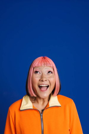 Téléchargez les photos : Asiatique fille avec des cheveux roses et piercing exprimant surprise à la caméra isolé sur fond bleu - en image libre de droit