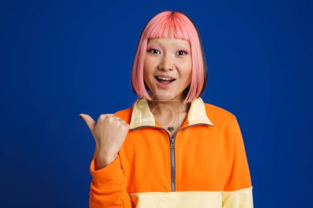Téléchargez les photos : Asiatique surprise fille avec des cheveux roses pointant doigt isolé sur fond bleu - en image libre de droit