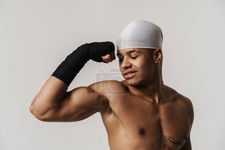 Téléchargez les photos : Jeune sportif torse nu souriant tout en montrant son biceps à la caméra isolé sur fond blanc - en image libre de droit