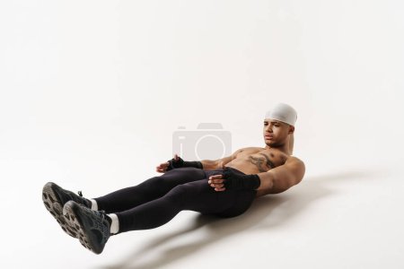 Téléchargez les photos : Jeune sportif torse nu faisant de l'exercice tout en travaillant isolé sur fond blanc - en image libre de droit