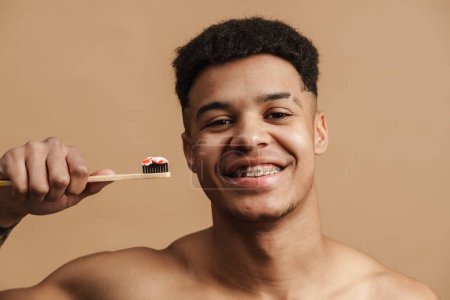 Foto de Joven hombre sin camisa sonriendo mientras posando con cepillo de dientes aislado sobre fondo beige - Imagen libre de derechos