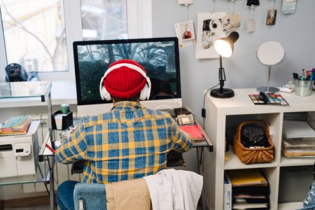 Téléchargez les photos : Adolescent garçon avec casque jouer jeu vidéo sur ordinateur de bureau à la maison - en image libre de droit