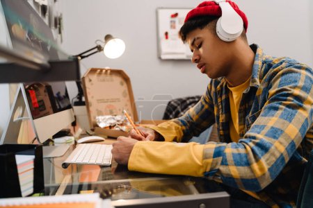Téléchargez les photos : Moyen-Orient adolescent garçon en utilisant ordinateur de bureau tout en étudiant à la maison - en image libre de droit
