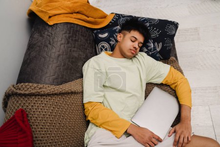 Photo for Brunette teenage boy sleeping while lying on couch with laptop in bedroom - Royalty Free Image