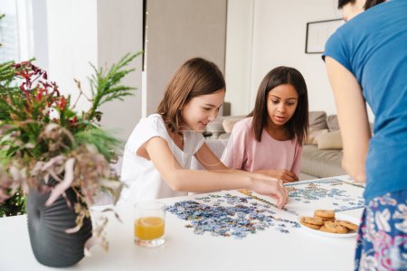Photo for Multiracial sisters doing puzzle together while spending time with their mother at home - Royalty Free Image