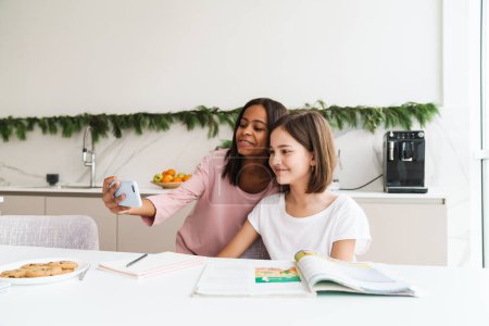 Photo for Multiracial sisters taking selfie photo while doing homework together at home - Royalty Free Image