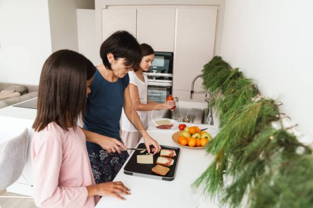 Téléchargez les photos : Sœurs multiraciales faisant des sandwichs avec leur mère dans la cuisine à la maison - en image libre de droit