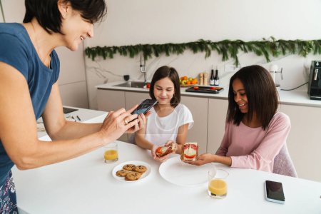 Téléchargez les photos : Femme blanche prenant des photos des sandwichs de sa fille dans la cuisine à la maison - en image libre de droit