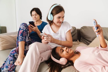 Photo for White woman and her daughters using gadgets while resting on couch at home - Royalty Free Image