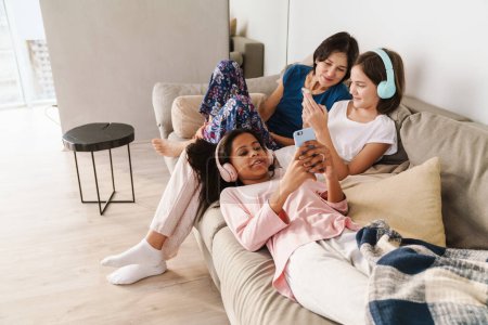Photo for White woman and her daughters using gadgets while resting on couch at home - Royalty Free Image