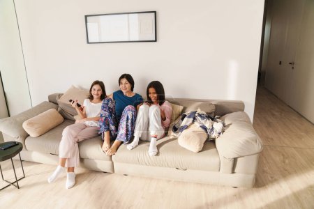 Téléchargez les photos : Femme blanche et ses filles regardant la télévision tout en se reposant sur le canapé à la maison - en image libre de droit