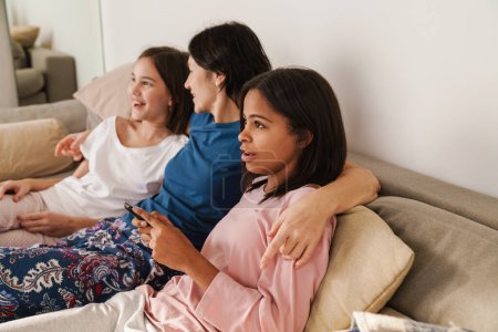 Photo for White woman and her daughters watching tv while resting on couch at home - Royalty Free Image