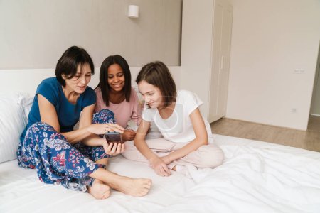 Téléchargez les photos : Femme blanche et ses filles utilisant des téléphones cellulaires tout en se reposant sur le lit à la maison - en image libre de droit