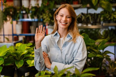 Téléchargez les photos : Blanc belle jeune fleuriste fille souriant tout en travaillant dans la boutique de fleurs - en image libre de droit