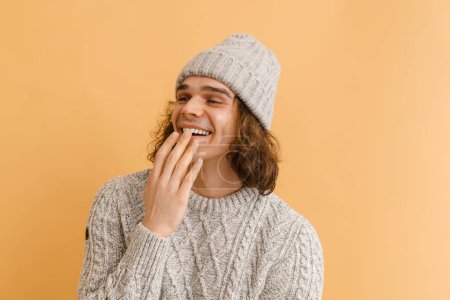 Foto de Joven hombre guapo con el pelo largo riendo y cubriendo su boca sobre fondo marrón aislado - Imagen libre de derechos