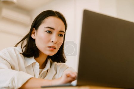 Téléchargez les photos : Jeune femme asiatique concentrée mignonne tendue avec ordinateur portable regardant à l'écran - en image libre de droit