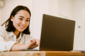 Young cute smiling asian woman with laptop looking on the screen Poster #625652532