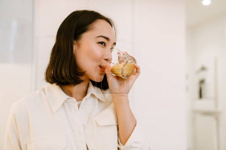 Téléchargez les photos : Jeune mignonne belle asiatique fille boire smoothie dans confortable cuisine à la maison - en image libre de droit