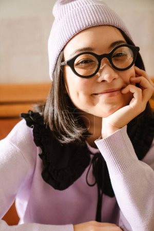 Photo for Young asian woman in eyeglasses smiling and looking at camera indoors - Royalty Free Image