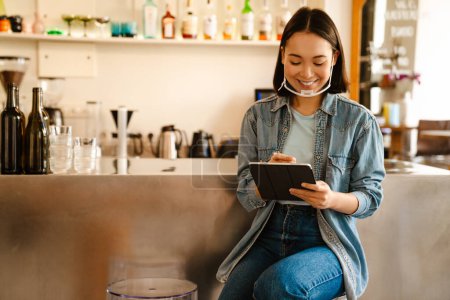 Téléchargez les photos : Jeune asiatique serveuse femme souriant tout en travaillant avec tablette informatique dans le café - en image libre de droit