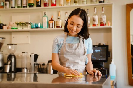 Téléchargez les photos : Jeune asiatique barista femme portant tablier souriant tout en travaillant dans café - en image libre de droit