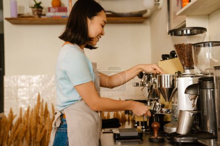 Photo for Young asian barista woman wearing apron smiling while making coffee in cafe - Royalty Free Image