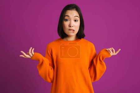 Téléchargez les photos : Perplexe asiatique femme fronçant les sourcils tout en gesticulant isolé sur fond violet - en image libre de droit