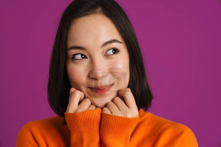Foto de Joven asiático mujer usando suéter sonriendo y mirando a un lado aislado sobre púrpura fondo - Imagen libre de derechos