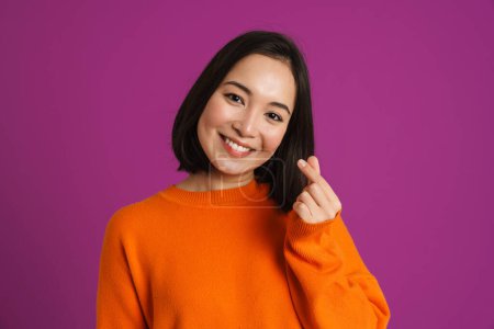 Téléchargez les photos : Jeune femme asiatique souriant et frottant ses doigts isolés sur fond violet - en image libre de droit