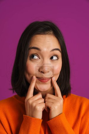 Téléchargez les photos : Asiatique femme regardant caméra tout en pointant les doigts à son sourire isolé sur fond violet - en image libre de droit