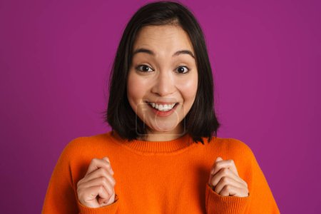 Téléchargez les photos : Femme asiatique excitée souriant et tenant les poings serrés isolés sur fond violet - en image libre de droit