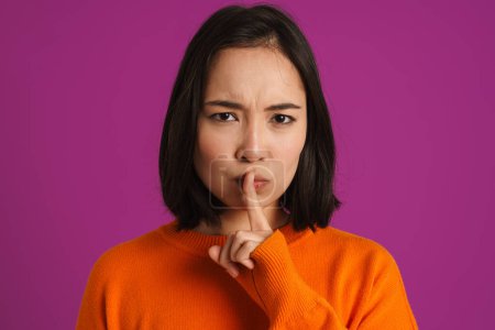 Téléchargez les photos : Jeune femme asiatique fronçant les sourcils tout en faisant un geste de silence isolé sur fond violet - en image libre de droit