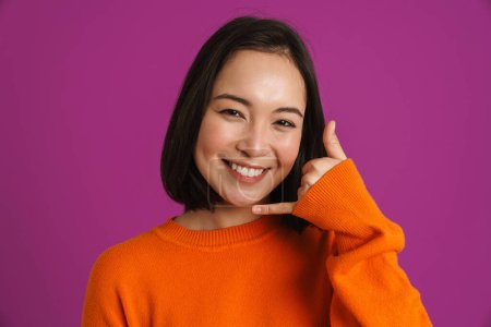 Foto de Joven mujer asiática sonriendo y haciendo gesto de teléfono aislado sobre fondo púrpura - Imagen libre de derechos
