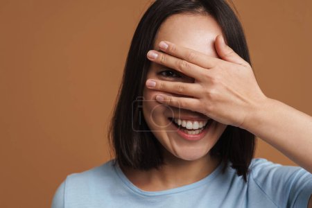 Photo for Young asian woman wearing t-shirt laughing and covering her eyes isolated over beige background - Royalty Free Image