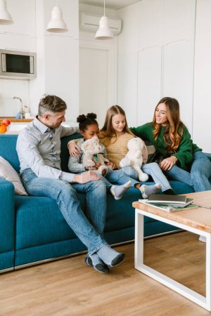Foto de Familia feliz sentado en el sofá, hermanas adoptadas jugando con juguetes de peluche en la amplia sala de estar en casa. Concepto de adopción. - Imagen libre de derechos