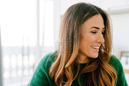 Téléchargez les photos : Adulte belle femme souriante en pull vert regardant de côté - en image libre de droit