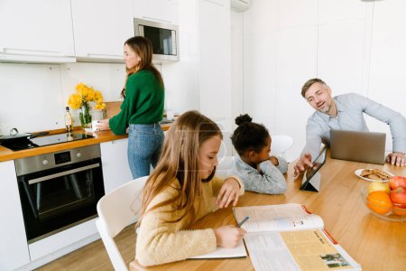 Photo for Happy family on cozy kitchen at home. Mother doing housework , working father with studying daughters sitting at the table - Royalty Free Image