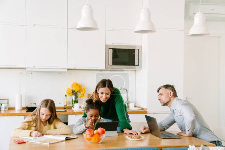 Photo for Happy family on cozy kitchen at home, mother and working father helping their daughters with homework - Royalty Free Image