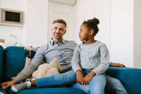 Photo for Happy smiling father sitting on couch with cute daughter. Adoption concept - Royalty Free Image