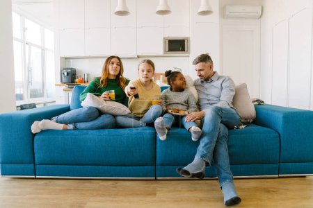 Foto de Feliz madre familiar, padre y dos hijas sentados en el sofá y viendo la televisión en casa. Concepto de adopción - Imagen libre de derechos