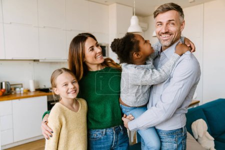 Foto de Familia feliz en la acogedora cocina en casa. Padre, madre y dos hijas. Concepto de adopción - Imagen libre de derechos