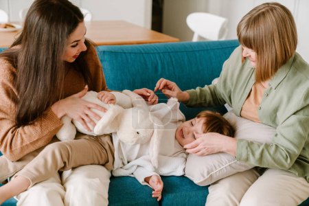 Téléchargez les photos : Fille blanche jouer avec sa mère et sa petite-fille sur le canapé à la maison - en image libre de droit