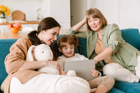 Téléchargez les photos : Fille blanche utilisant un ordinateur tablette tout en passant du temps avec sa famille à la maison - en image libre de droit