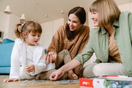 Photo for White blonde girl completing puzzle with her family at home - Royalty Free Image