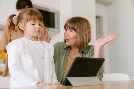 Téléchargez les photos : Fille blanche utilisant un ordinateur tablette tout en passant du temps avec sa famille à la maison - en image libre de droit
