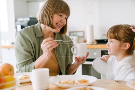 Téléchargez les photos : Blanc fille blonde prendre le petit déjeuner avec sa grand-mère à la maison - en image libre de droit
